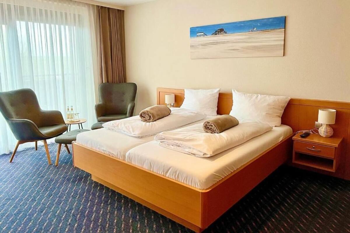 Ein Hotelzimmer mit einem Bett, zwei Stühlen, einem Nachttisch, einer Lampe und einem Bild an der Wand.