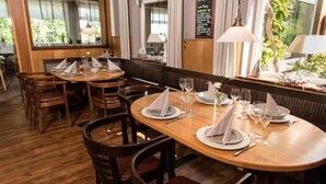 Een restaurant met houten tafels en stoelen, gedekt met borden, glazen en bestek.