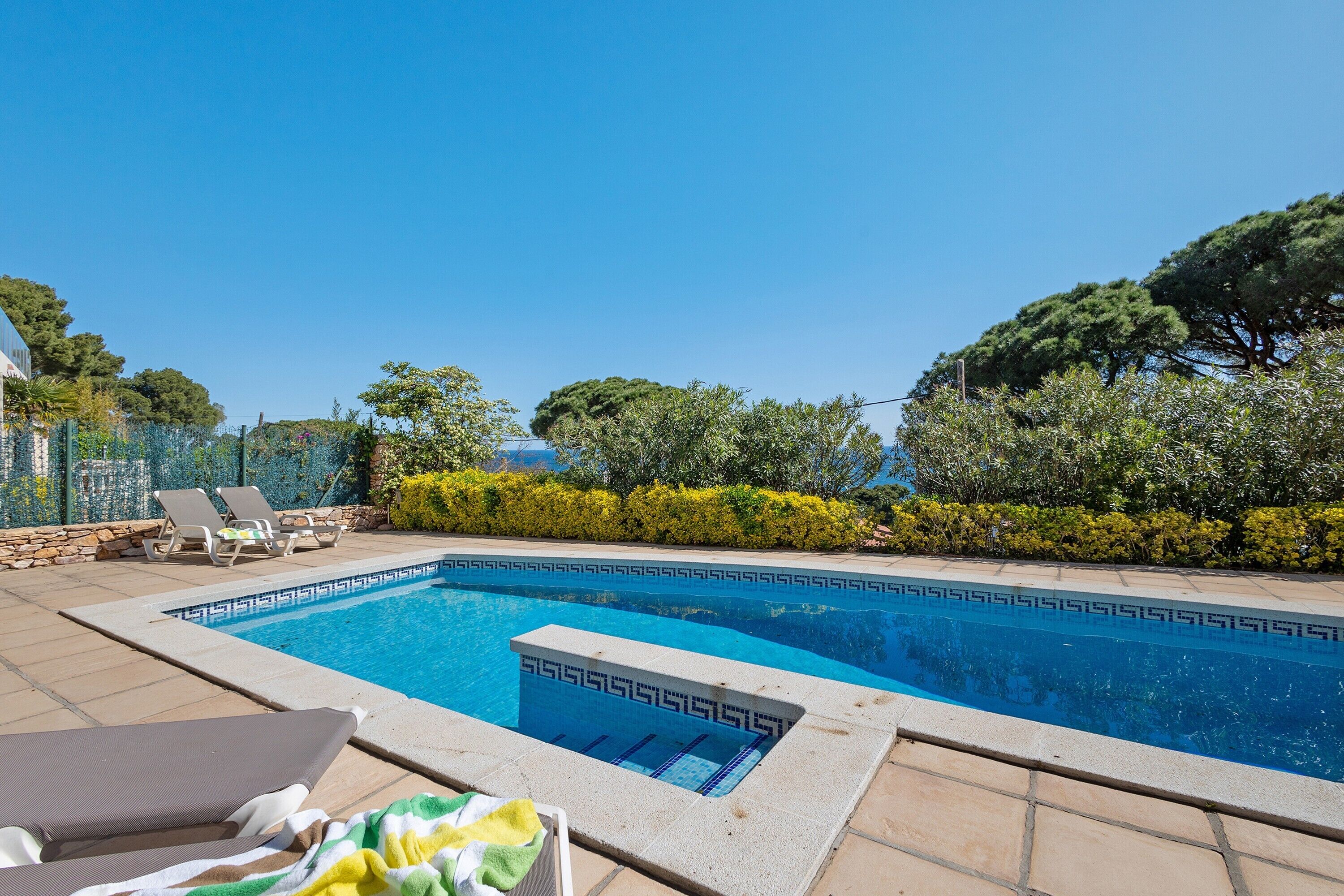 Une piscine dont le fond est recouvert de carreaux formant un motif géométrique, entourée d’une terrasse carrelée et de chaises longues.