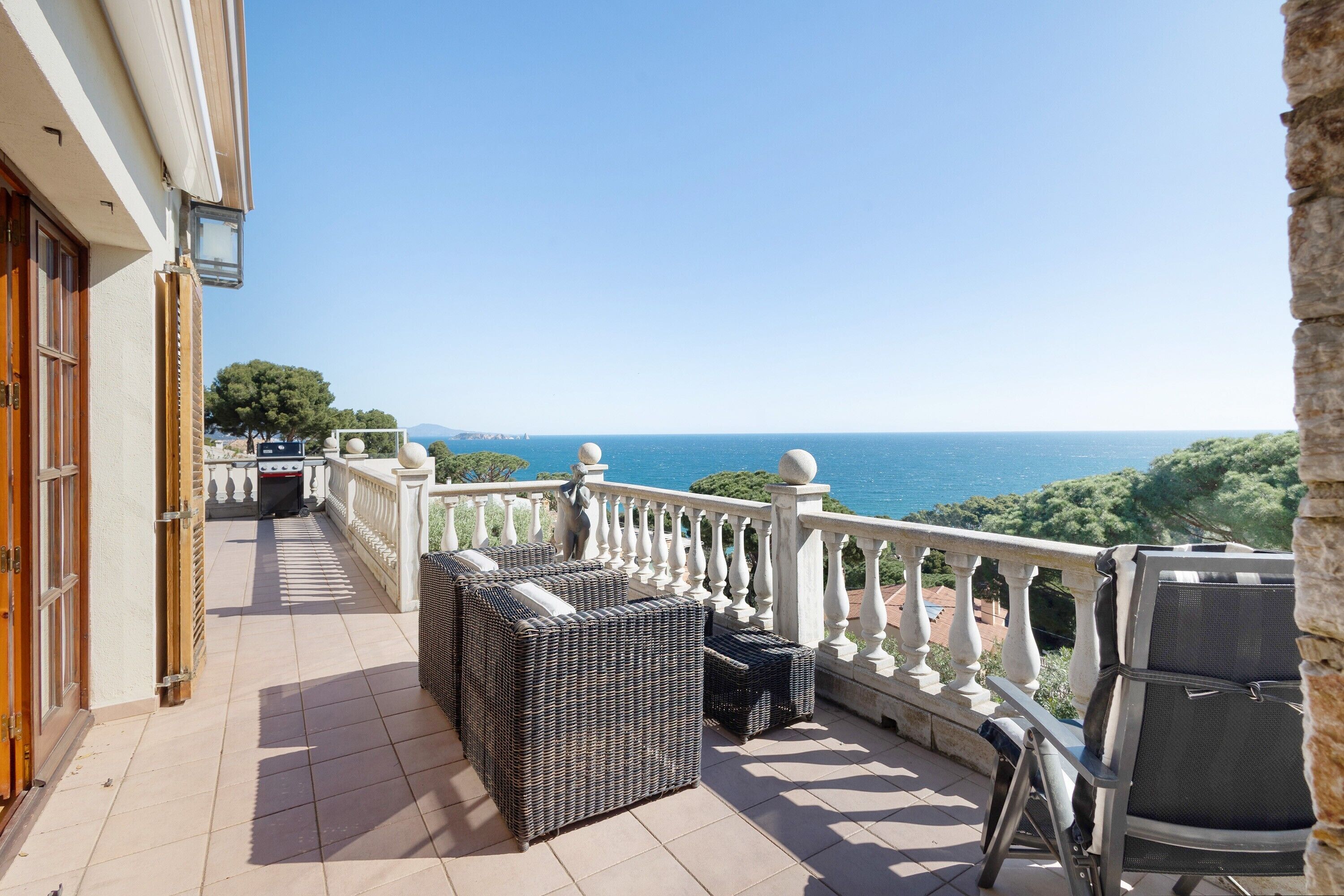 A balcony with wicker furniture, a grill, and a view of the sea.