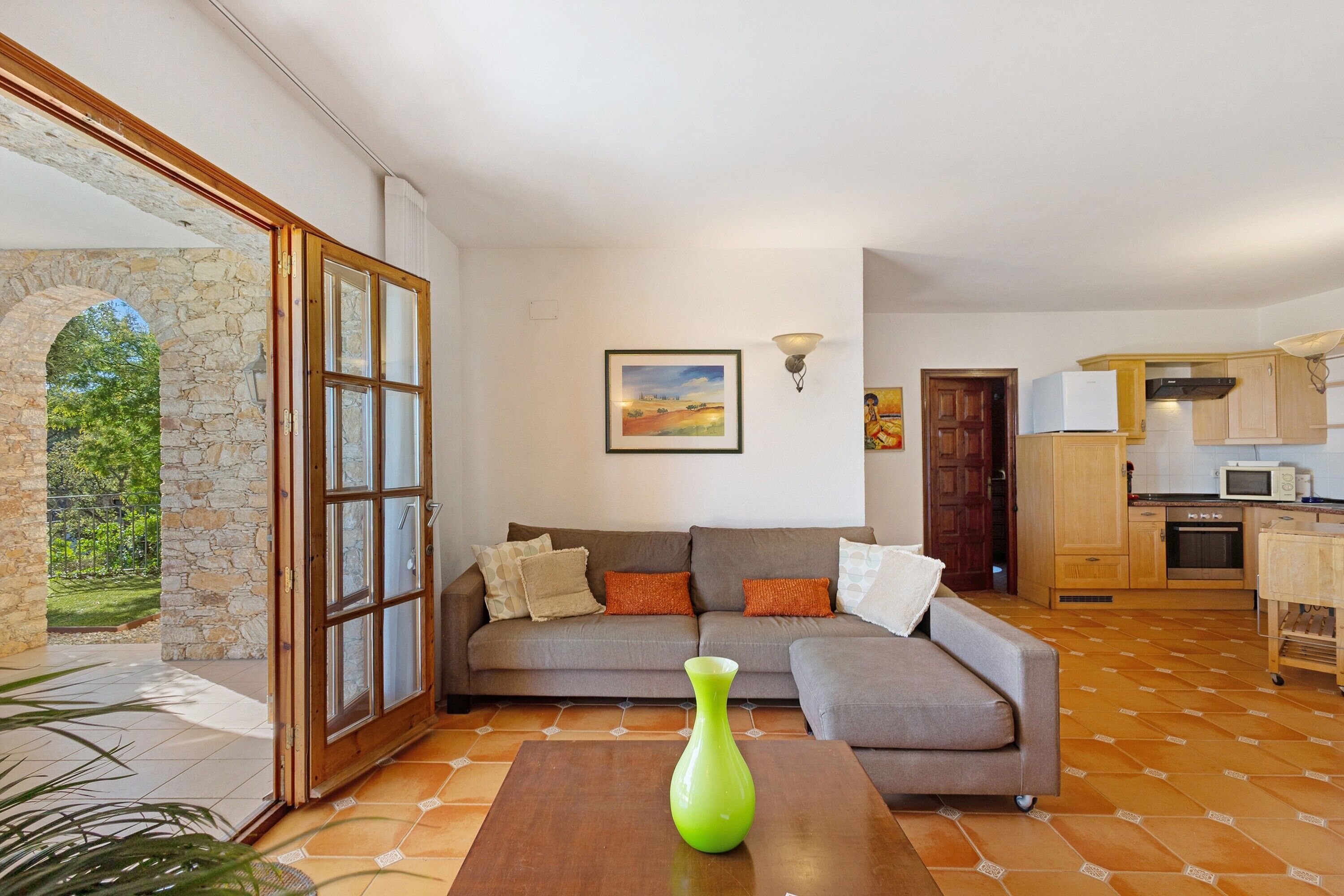 A living room with a sofa, a green vase, and a kitchen in the background.