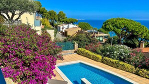 A swimming pool with lounge chairs, surrounded by lush greenery and a view of the sea. - Fantastic Villa with Pool and Spectacular Sea Views (Sa Riera)