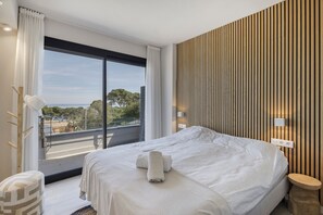 A hotel room with a large bed, a view of the outdoors, a wooden wall panel, and a bedside table. - Spectacular Duplex with Stunning Sea Views (Begur)