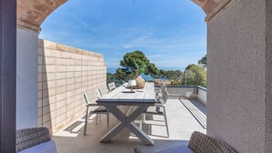 Eine Terrasse im Freien mit Tisch und Stühlen, Blick auf das Meer und eine Steinmauer.