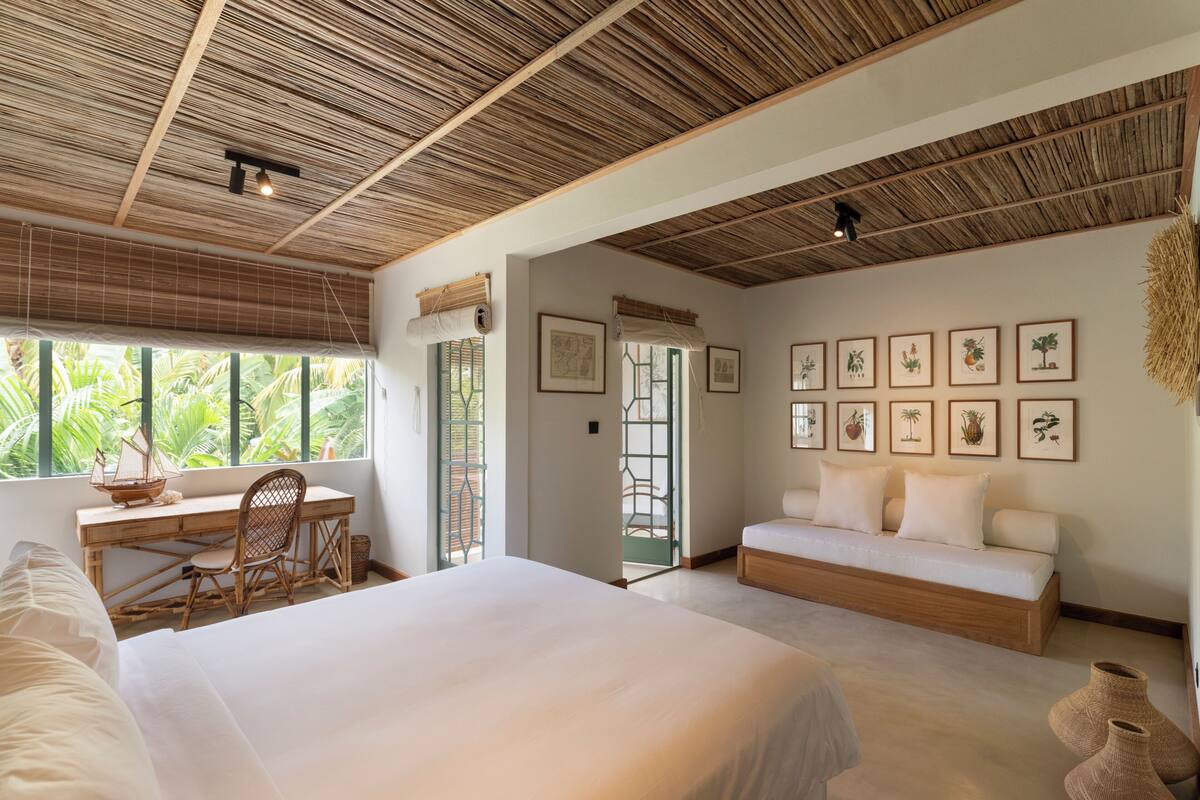 Un dormitorio con una cama grande, un escritorio, un sofá e impresiones enmarcadas de motivos botánicos en la pared.