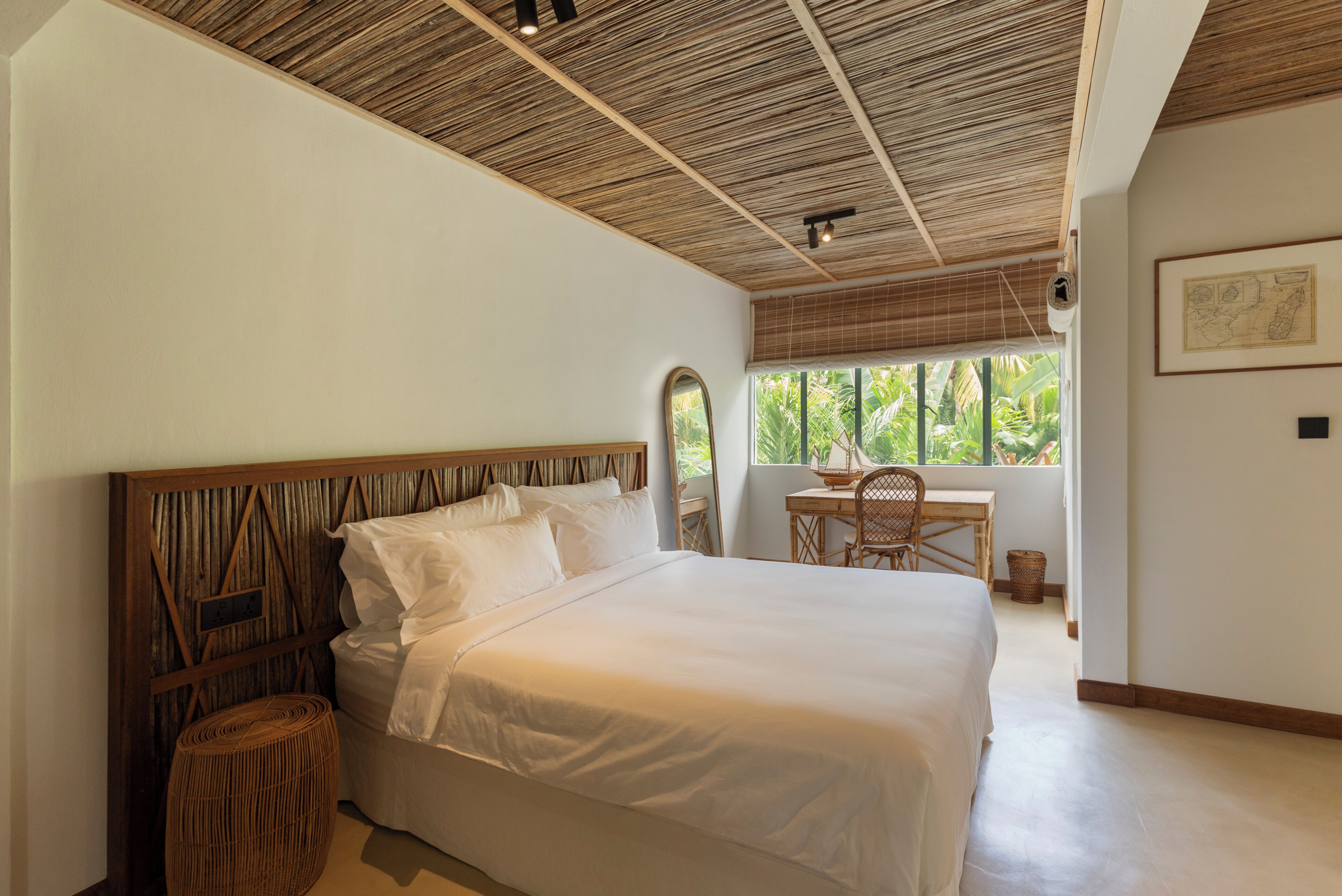 Ein Schlafzimmer mit einem großen Bett, einem Holzkopfende, einem kleinen Tisch und einem Fenster mit Blick auf Grünflächen.