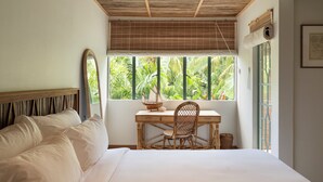 Un dormitorio con cama, escritorio y silla, una ventana con vistas a follaje, y un techo con diseño de madera.