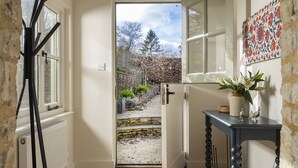 Ein Durchgang zu einem Garten mit einer Steinsäule, einem kleinen Tisch mit Blumen in einer Vase und einer Wand mit gemusterten Fliesen.