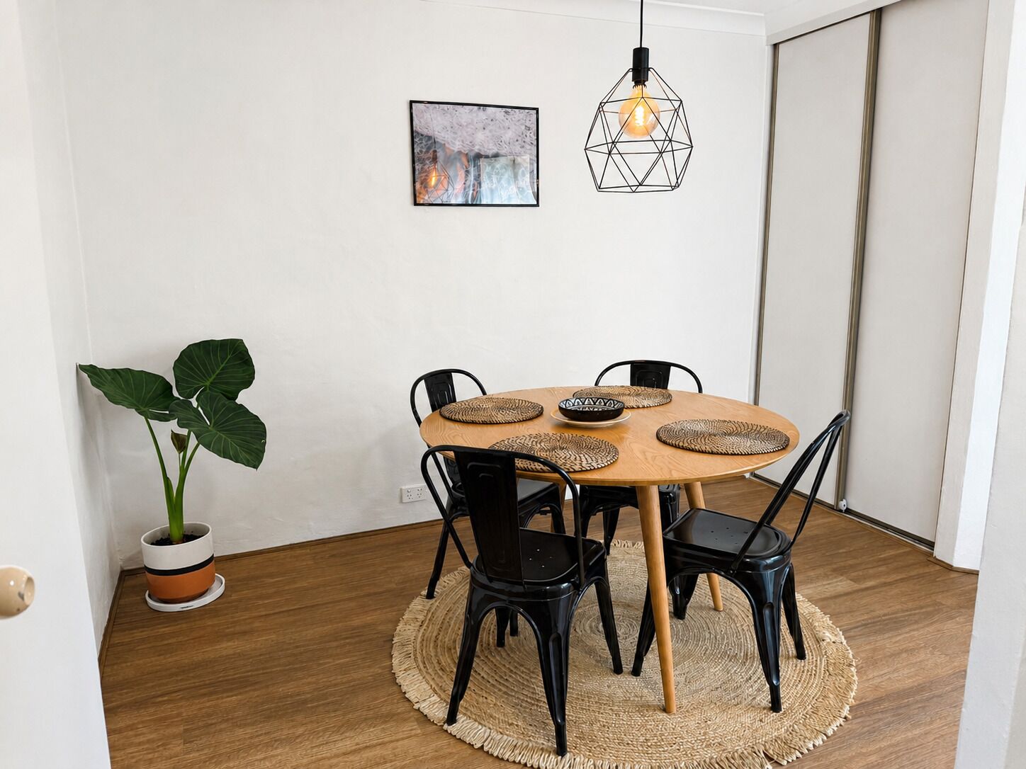 A dining area with a round table, black chairs, woven placemats, and a hanging light fixture.