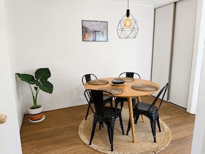 A dining area with a round table, black chairs, woven placemats, and a hanging light fixture. - Stylish two-bedroom, resort-style apartment for up to four guests, five minutes from Fremantle city centre. Unwind with a king bed, two private balconies, shared pool, fast Wi-Fi, split-system air-conditioning and heating, and free undercover parking (Fremantle)