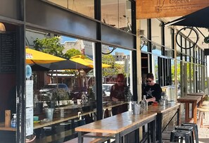 A café with a menu board, outdoor seating, and a bar area. - Stylish two-bedroom, resort-style apartment for up to four guests, five minutes from Fremantle city centre. Unwind with a king bed, two private balconies, shared pool, fast Wi-Fi, split-system air-conditioning and heating, and free undercover parking (Fremantle)