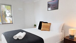 Una cama bien tendida con un edredón blanco y negro, dos toallas enrolladas y una mesita de noche con una lámpara.
