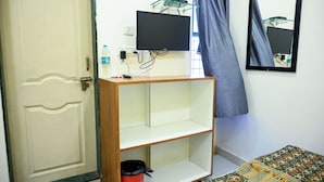 A room with a wooden shelf, a television mounted on the wall, a mirror, and a door. - hari krupa bhakta niwas (Jejuri)