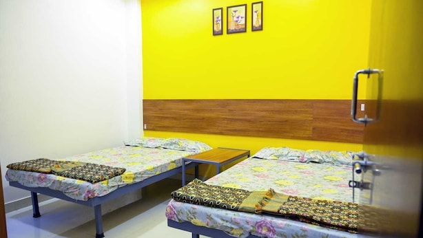 A room with two single beds, a wooden headboard, a small table, and a wall-mounted light fixture. - hari krupa bhakta niwas (Jejuri)