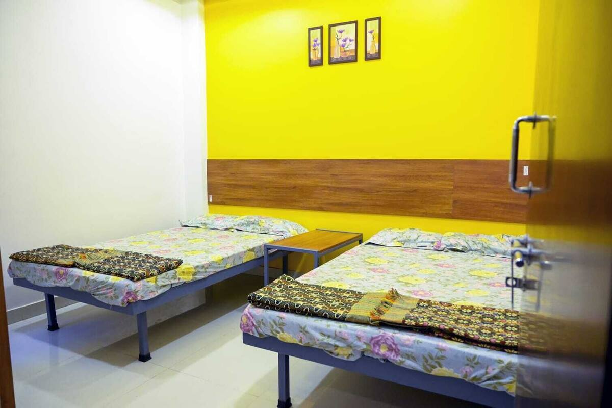 A room with two single beds, a wooden headboard, a small table, and a wall-mounted light fixture.