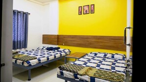 A room with two beds, a ceiling fan, and a yellow wall. - hari krupa bhakta niwas (Jejuri)