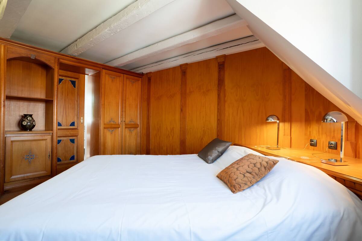 Un dormitorio con una cama grande, un armario de madera, mesita de noche, lámpara y un pequeño adorno en la mesita.