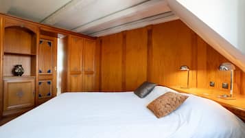 Un dormitorio con una cama grande, un armario de madera, mesita de noche, lámpara y un pequeño adorno en la mesita.