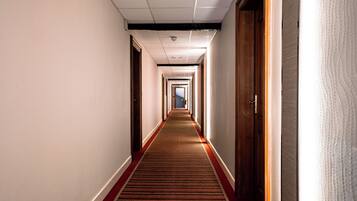A hotel corridor with a carpeted floor, wooden doors, and a ceiling with recessed lighting.