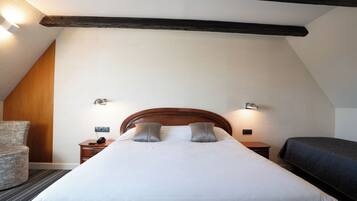 Una habitación de hotel con cabecera de madera, una cama individual con ropa blanca, una mesita de noche con teléfono y una silla.