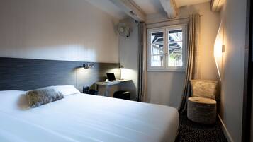 Habitación de hotel con cama, escritorio con computadora portátil, silla, ventana con cortinas y luz en la pared.