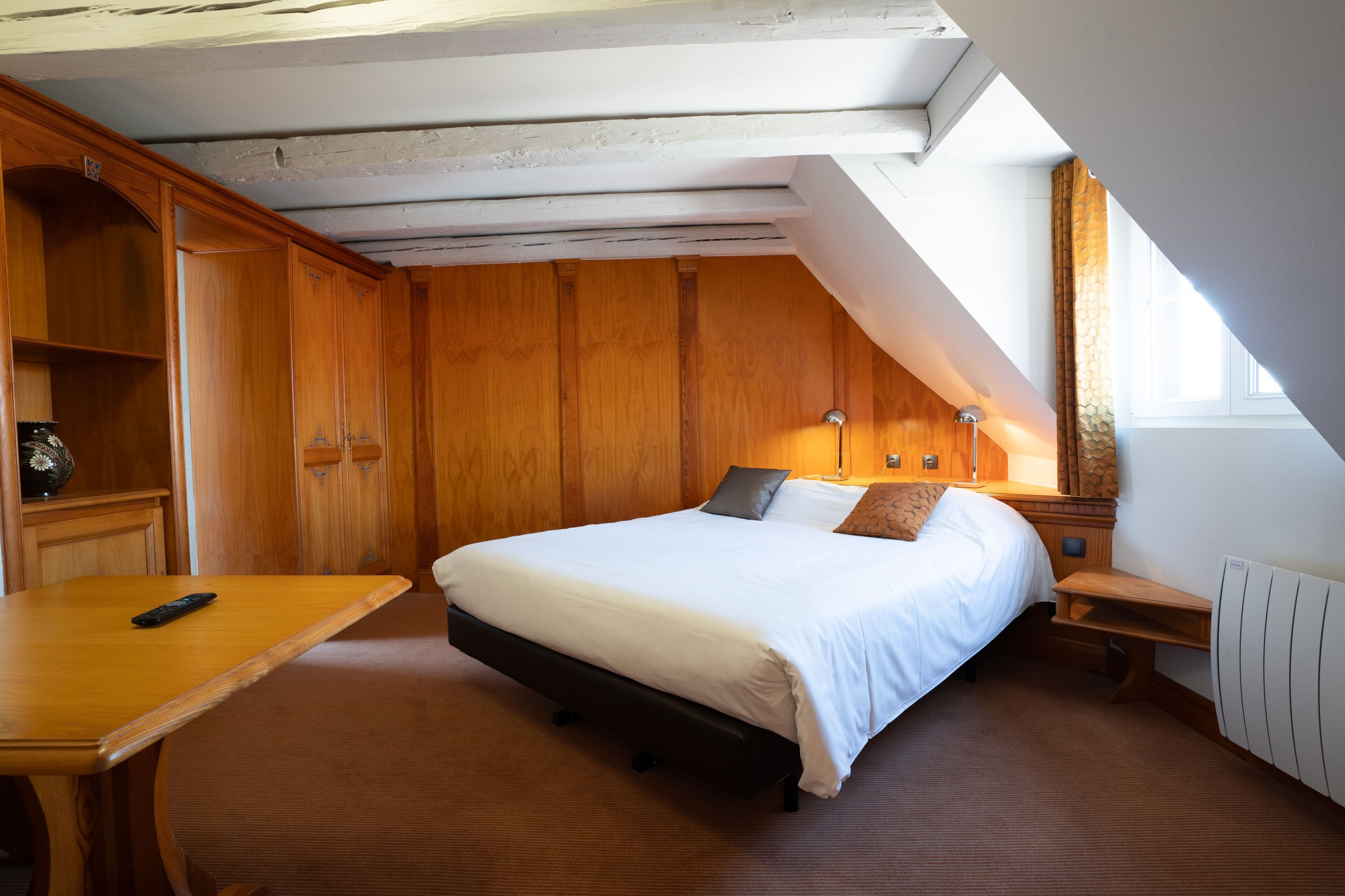 Un dormitorio con cama, armario de madera, mesita de noche y ventana.