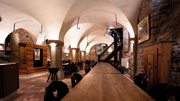 A long wooden table with chairs, a bar area, and stone walls with arched ceilings. - Hôtel Restaurant Père Benoît (Entzheim)