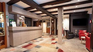 A hotel lobby with a reception desk, a clock, a television, and seating areas. - Hôtel Restaurant Père Benoît (Entzheim)
