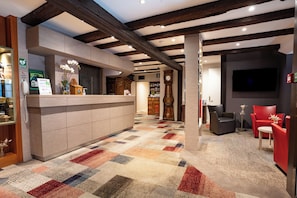Un hall d’hôtel comprenant un comptoir d’accueil, une horloge, un téléviseur et des espaces où s’asseoir.