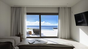Una camera moderna con un'ampia porta scorrevole in vetro che dà su un balcone con piscina e vista sull'oceano.