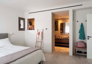 A bedroom with a bed, a ladder, a bathroom with a sink, and a shoe rack. - Luxury Mykonos Villa with Private Pool and Stunning Sea Views (MYKONOS)
