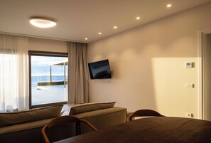 A modern room with a large window, a flat-screen TV, a dining table, and a sofa. - Luxury Mykonos Villa with Private Pool and Stunning Sea Views (MYKONOS)