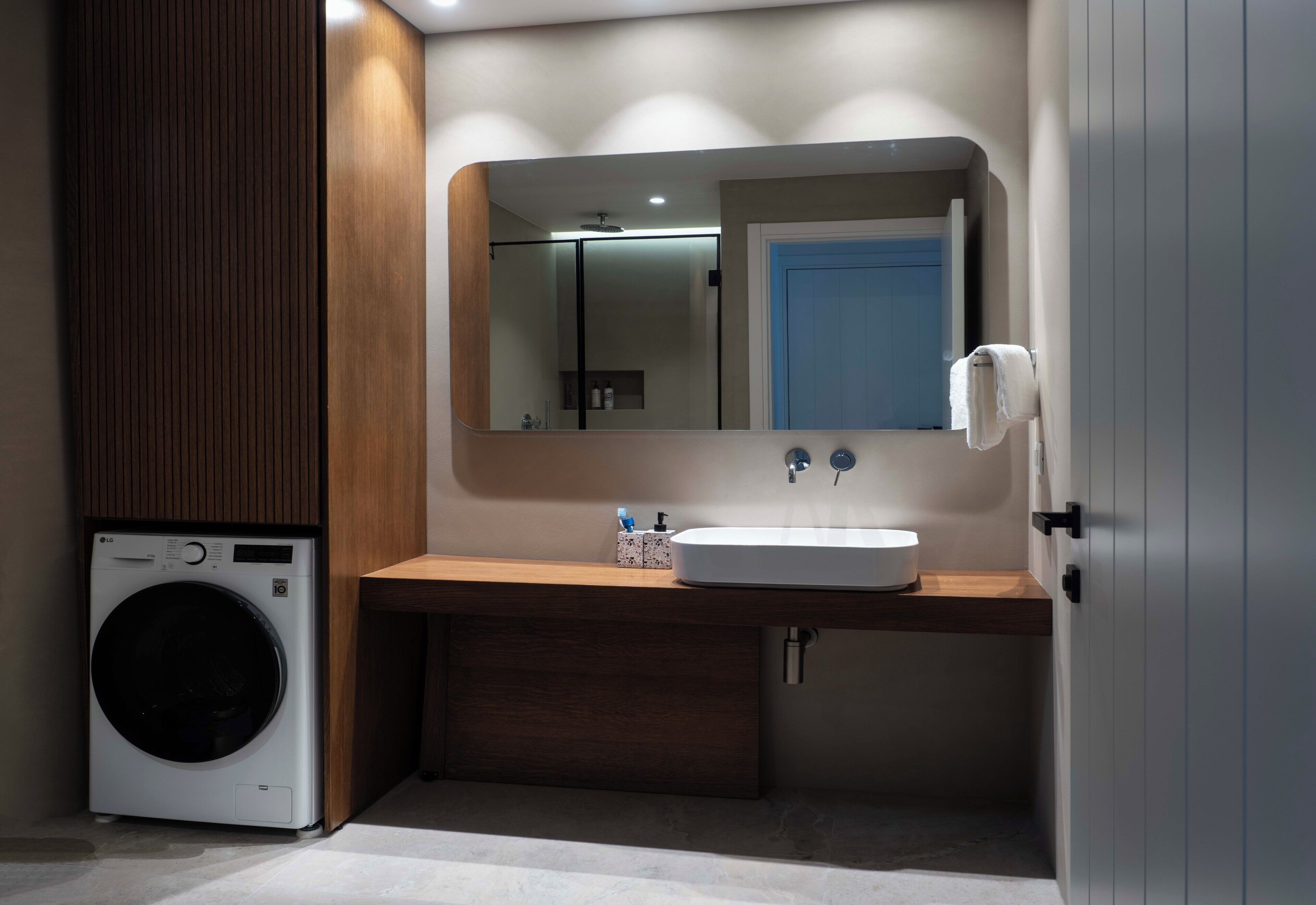 A compact bathroom with a washing machine, a sink, and a mirror.