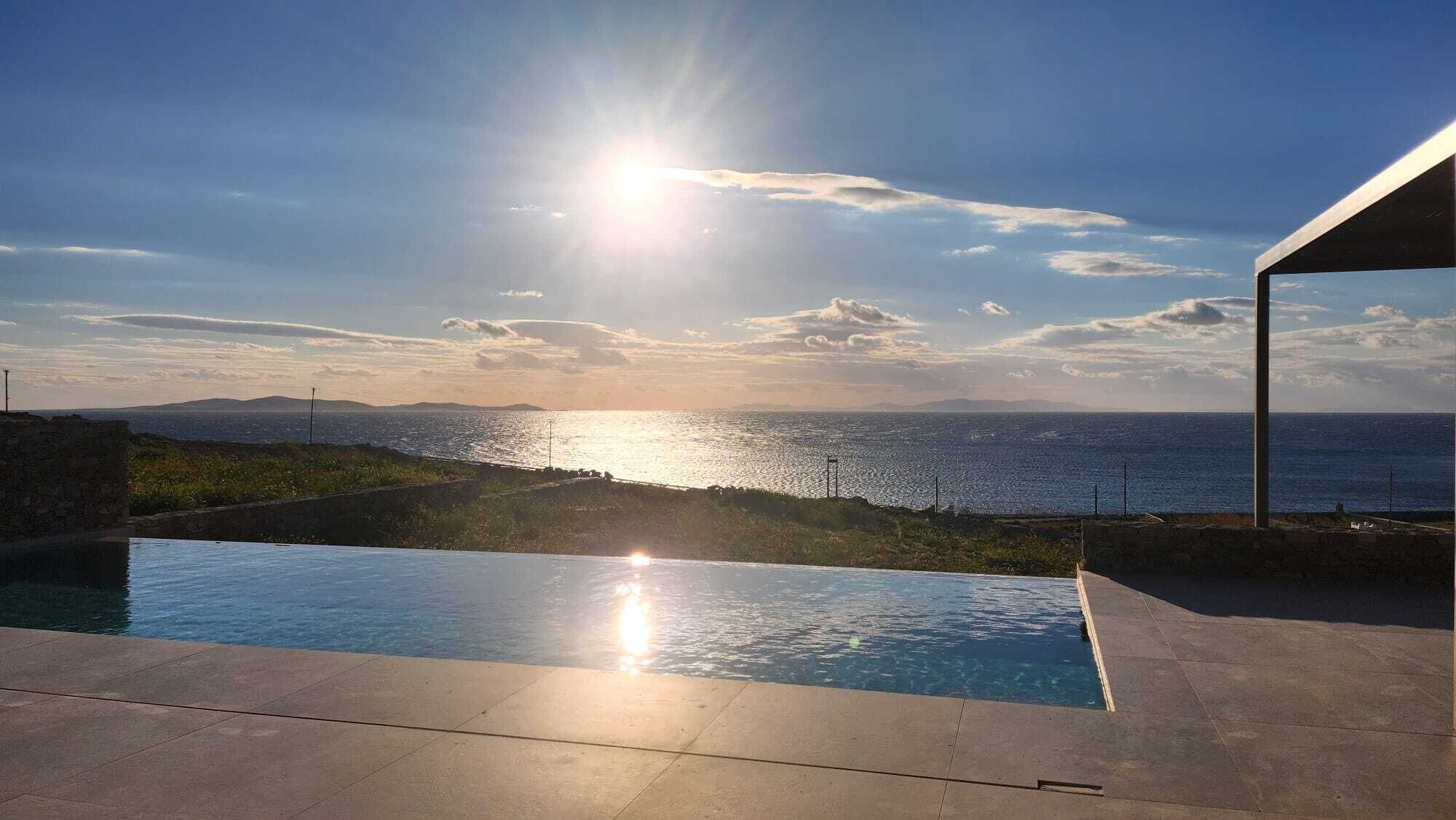 Une piscine offrant une vue sur la mer et les montagnes au coucher du soleil.
