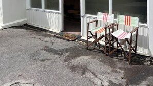 En vit byggnad med stora fönster, en liten veranda och en metallstege.