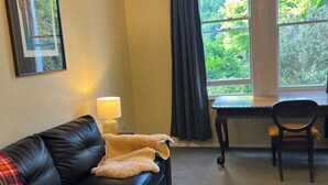 Ett rum med en svart lädersoffa, ett bord, en stol, en lampa och ett fönster med gardiner.