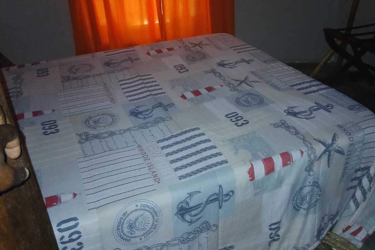 Una cama con una colcha estampada, cabecera de madera y una silla de mimbre.