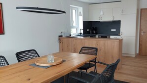 Een moderne keuken met houten kastjes, een centraal eiland, zwarte stoelen en een eettafel met een glazen decoratie.