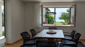Een eetgedeelte met een tafel, stoelen, een hanglamp en een groot raam met een open gordijn.