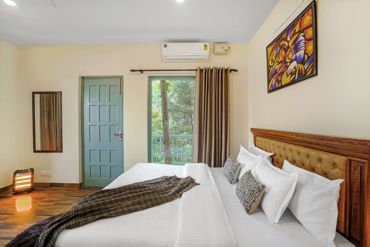 A hotel room with a bed, a door, an air conditioner, a painting, and a window with curtains.