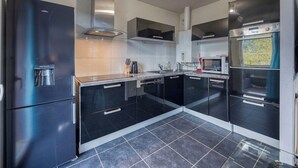 Une cuisine moderne avec des meubles de couleur noire, des appareils électroménagers en acier inoxydable et un sol carrelé.
