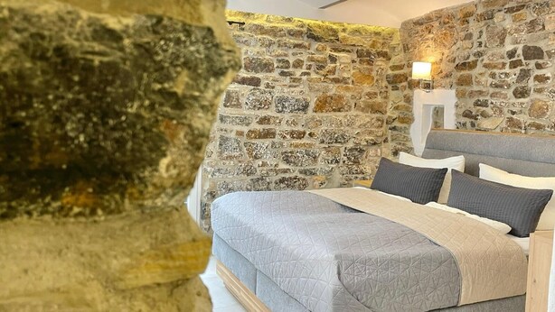 Un dormitorio con pared de piedra, una cama con ropa de cama gris y una mesita de noche con lámpara.