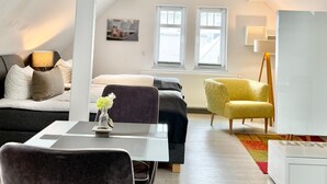 Una habitación moderna estilo loft con cama en entrepiso, sofá, mesa de comedor y un sillón amarillo.