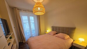 Ein Schlafzimmer mit Bett, Nachttischlampen, einem Fernseher und einem Fenster mit Vorhängen.
