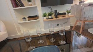 Ein Wohnzimmer mit Glastisch, Flachbildfernseher, Bücherregal und Essbereich mit einem Stuhl.