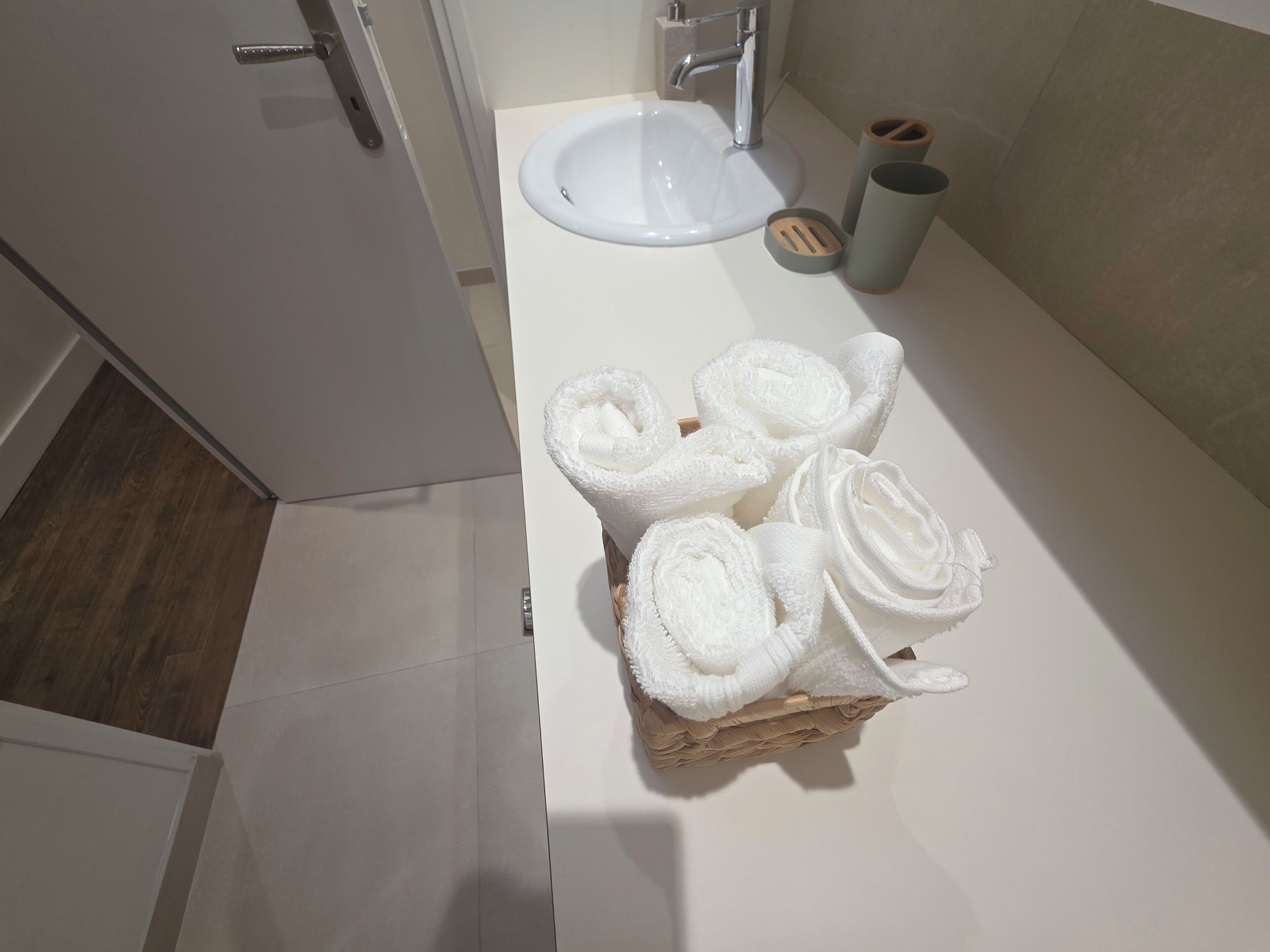 Een badkamer met een witte wasbak, een handdoekrek met opgerolde handdoeken en een houten vloer.