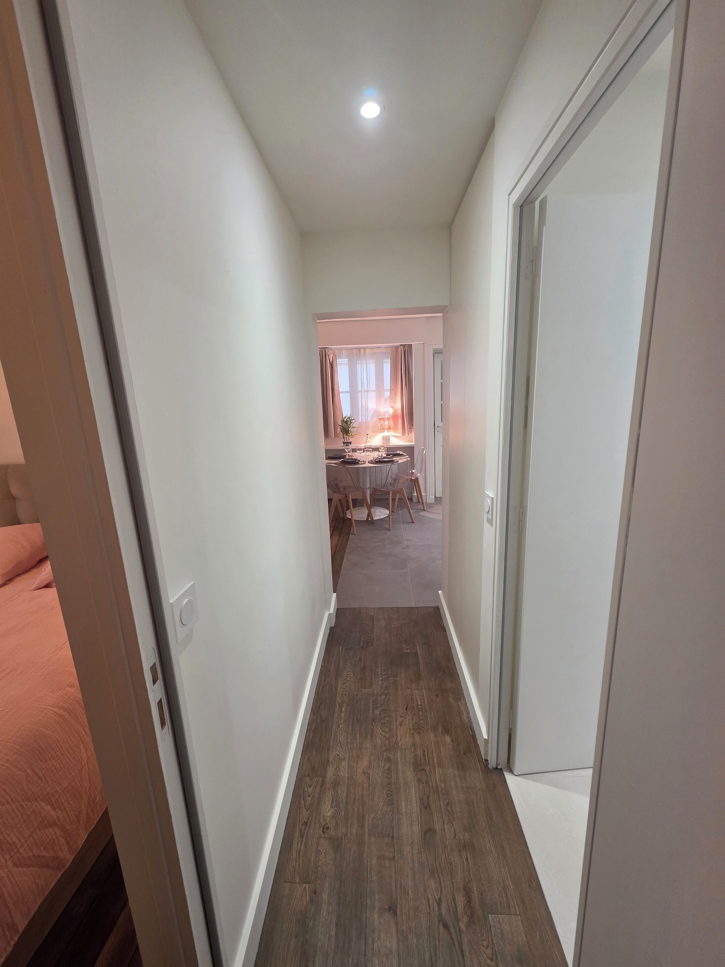 A narrow hallway with a wooden floor, leading to a room with a dining table and chairs.