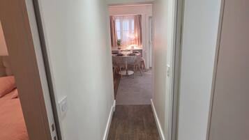 A narrow hallway with a wooden floor, leading to a room with a dining table and chairs.