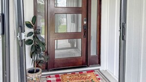 Een houten voordeur met een ruit, een bloempot en een welkomstmat.