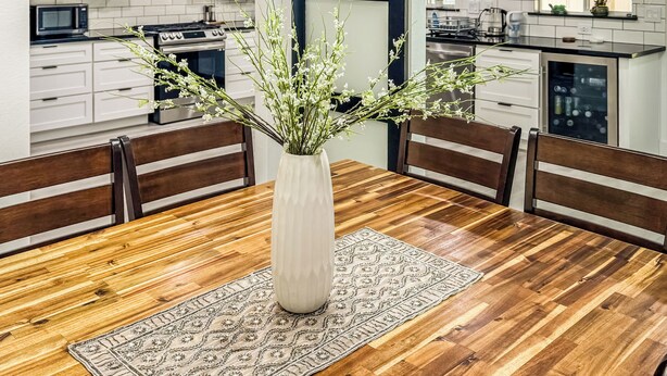 Een eetgedeelte met een houten tafel, een witte vaas met bloemen en een tapijt met een patroon.